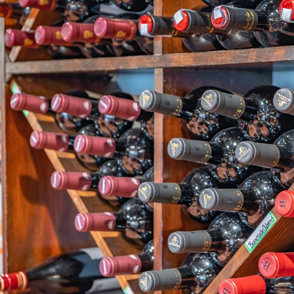 Rows of red wine bottles with red and black labels stored in wooden racks at Bella Napoli.