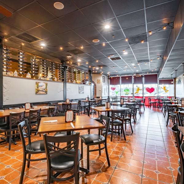 Interior of Bella Napoli Pizzeria & Restaurant with empty tables, wine racks, and tiled floors.