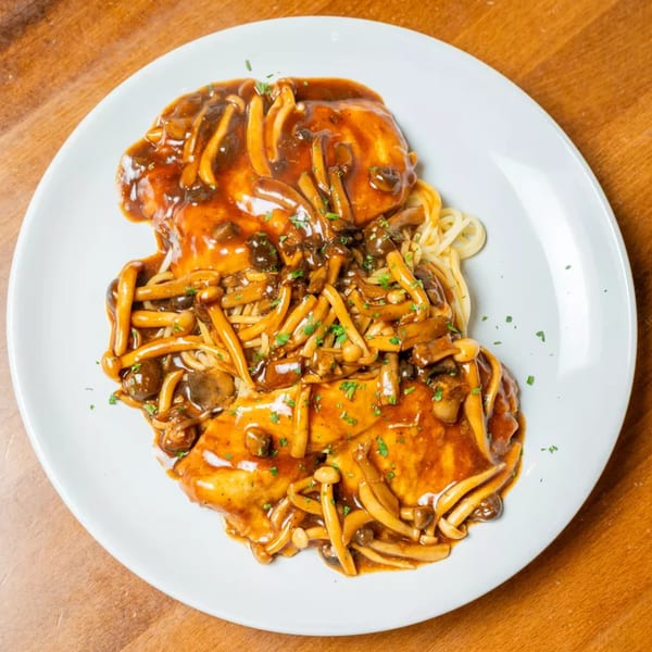 Chicken and pasta covered in a rich brown mushroom sauce, garnished with parsley on a white plate.