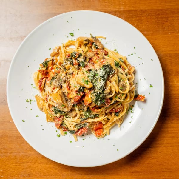 Linguine pasta with mushrooms, sun-dried tomatoes, spinach, and parmesan cheese on a white plate.