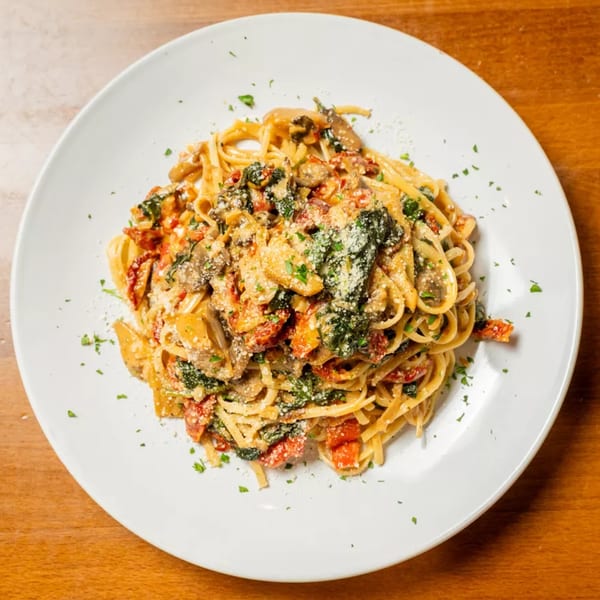 Linguine pasta with mushrooms, sun-dried tomatoes, spinach, and parmesan cheese on a white plate.