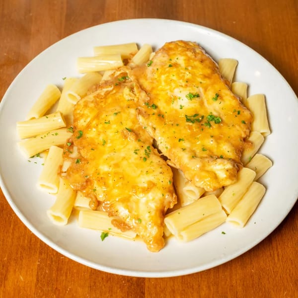 Chicken Francaise with rigatoni pasta, garnished with parsley, on a white plate.