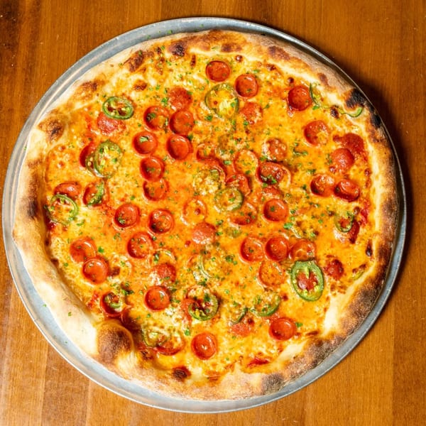 A whole pepperoni and jalapeño pizza, topped with herbs, on a metal pan over a wooden table.
