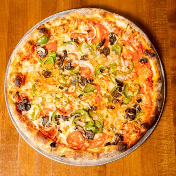 A whole pizza with melted cheese, green peppers, mushrooms, onions, and tomatoes on a wooden table.