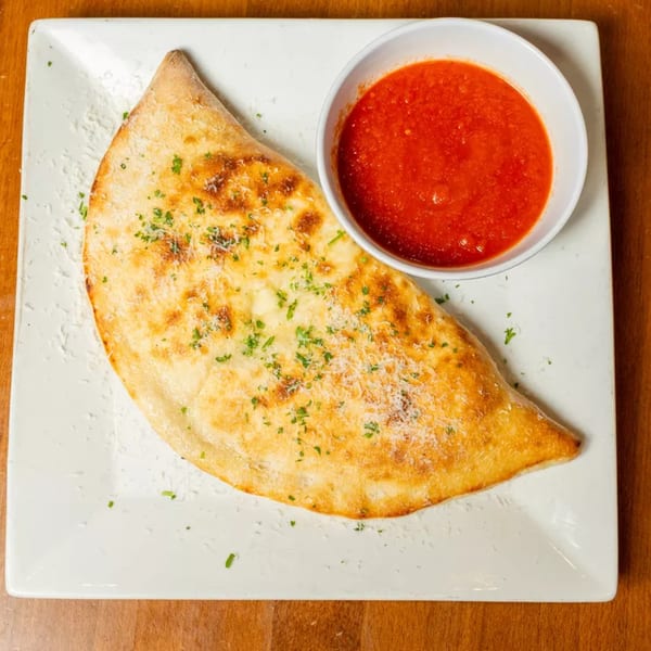 Golden-brown calzone sprinkled with herbs and cheese, served with a side of red marinara sauce.