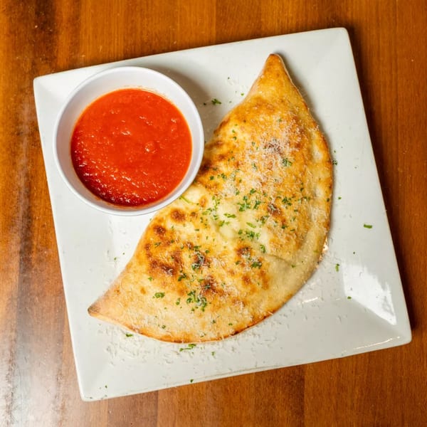 Golden-brown calzone with parmesan and parsley, served with a side of red marinara sauce.