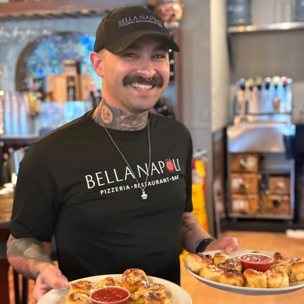 Smiling Bella Napoli staff member holding two plates of garlic knots with marinara sauce.