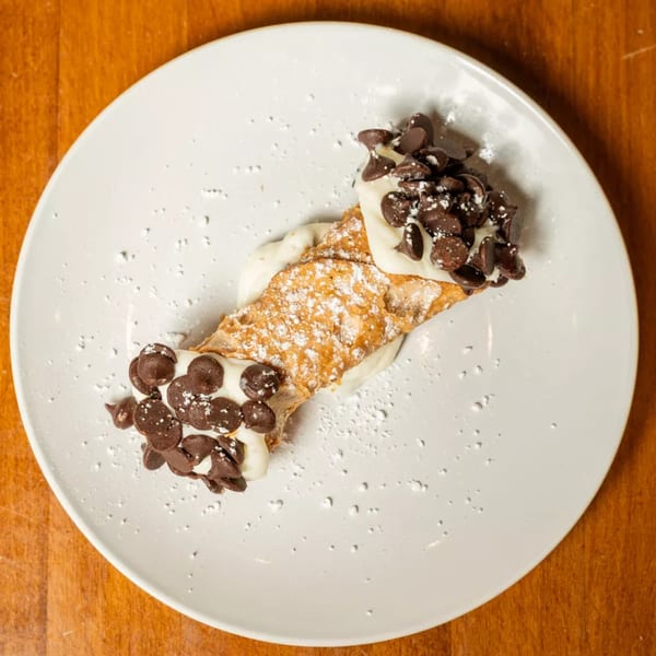 A cannoli filled with cream, topped with chocolate chips and powdered sugar on a white plate.