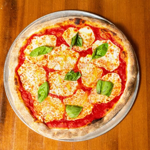 A whole Margherita pizza with fresh basil leaves, mozzarella, and tomato sauce on a metal tray.