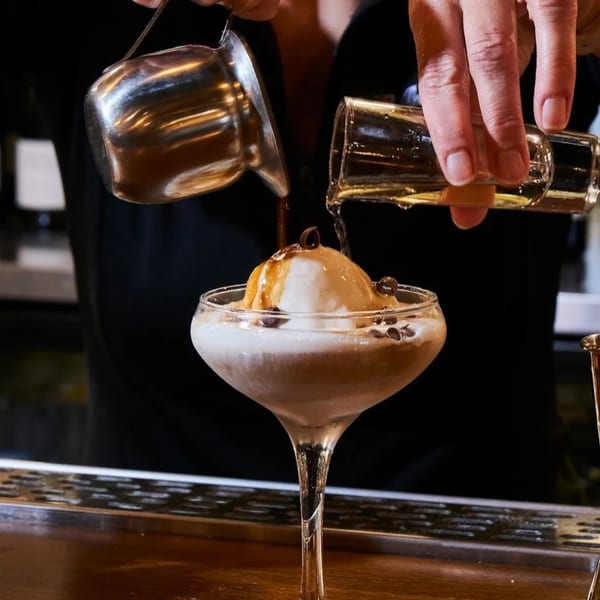 A person pouring espresso and liqueur over a scoop of vanilla gelato in a martini glass.