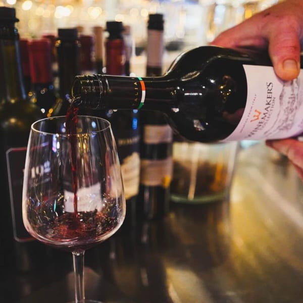 A hand pours red Italian wine from a bottle into a glass at Bella Napoli Pizzeria.