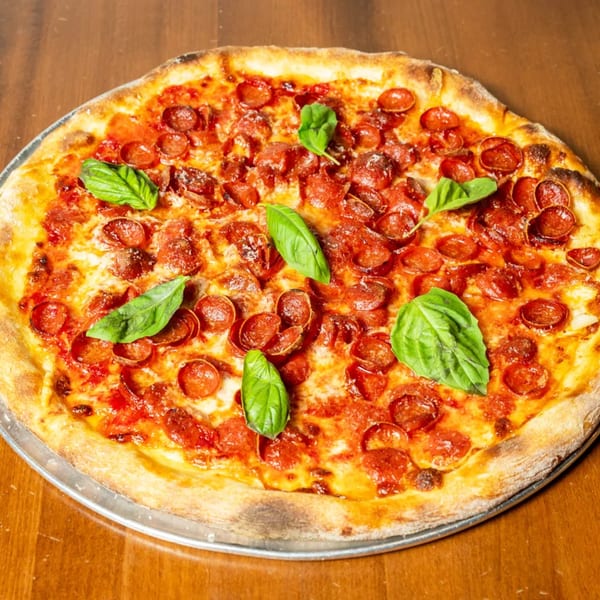 A whole pepperoni pizza with fresh basil leaves on a metal tray, on a wooden table.