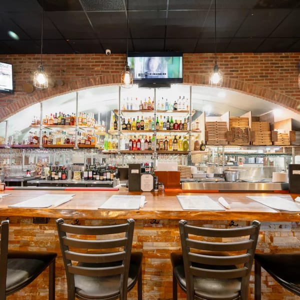 A rustic bar with brick arches, shelves of liquor bottles, and two empty bar stools.
