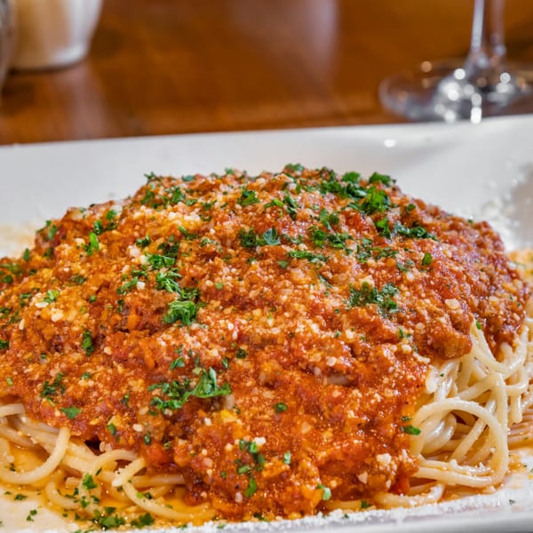 Spaghetti with rich red meat sauce, grated cheese, and fresh parsley on a white plate.
