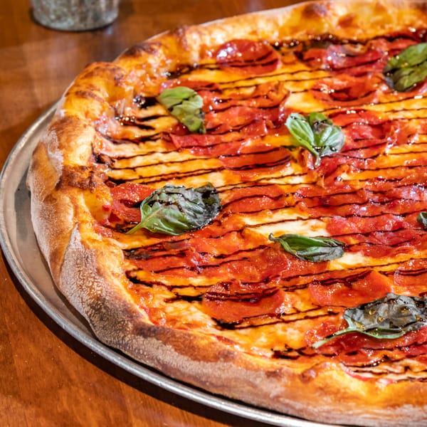 Bella Napoli Pizzeria's pepperoni pizza with fresh basil and balsamic glaze on a metal tray.