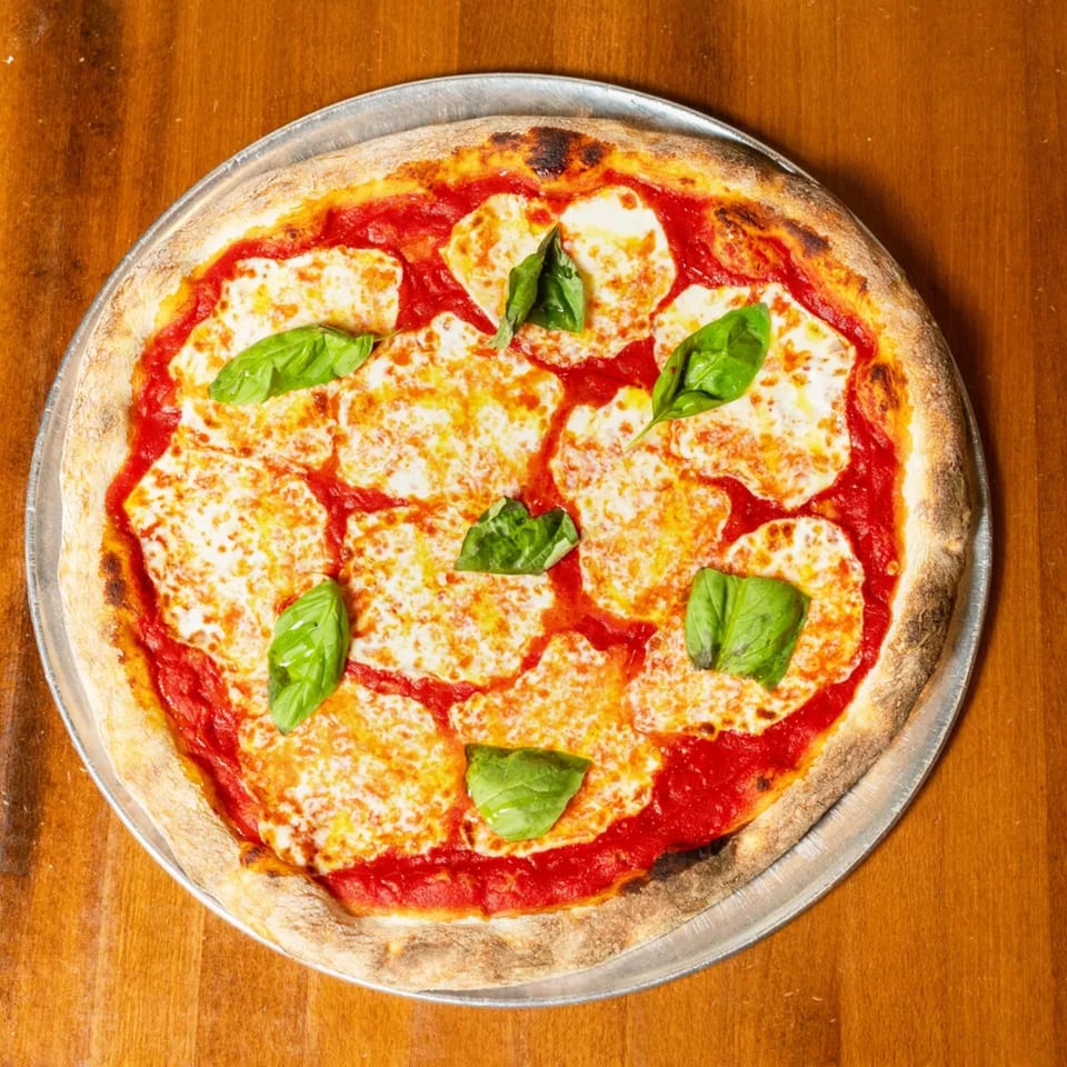 A freshly baked Margherita pizza with melted mozzarella, red sauce, and basil leaves on a wooden table.