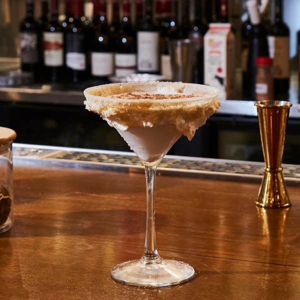 A martini glass with a creamy drink, sugar-rimmed, and sprinkled with cinnamon on a bar.