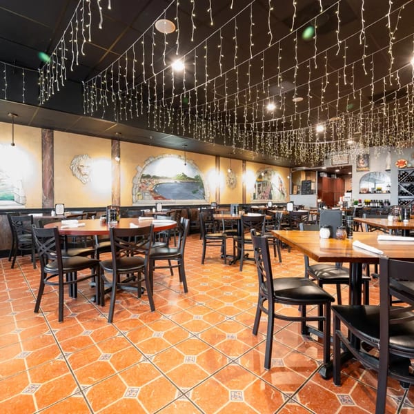 Restaurant dining room with warm lighting, murals, and many tables with black chairs.