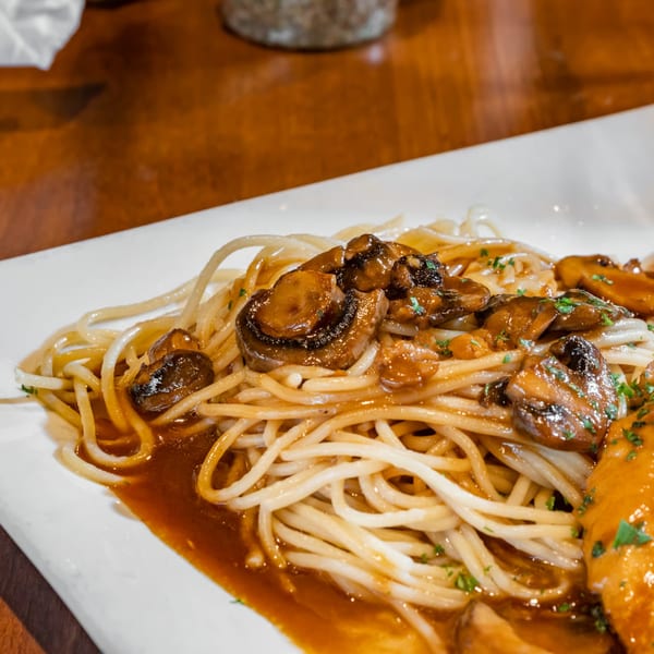 Spaghetti with mushrooms and a rich brown sauce, garnished with parsley on a white plate.