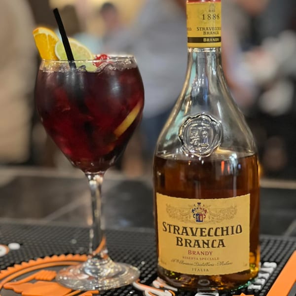 A glass of sangria with fruit and a bottle of Stravecchio Branca Brandy on a bar mat.