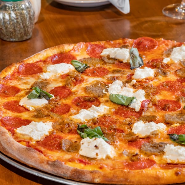 A Bella Napoli pepperoni, sausage, and ricotta pizza with basil on a wooden table.