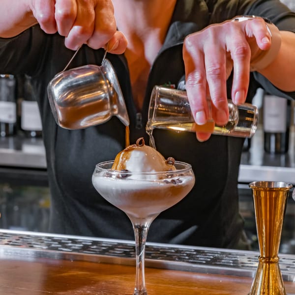 A bartender pours espresso and liquor over a scoop of gelato in a martini glass.
