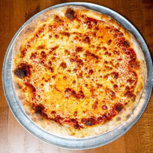 A freshly baked cheese pizza with a golden crust on a metal pan, on a wooden table.