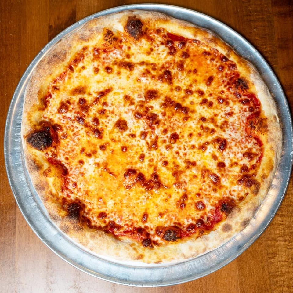 A freshly baked cheese pizza with a golden crust on a metal pan, on a wooden table.