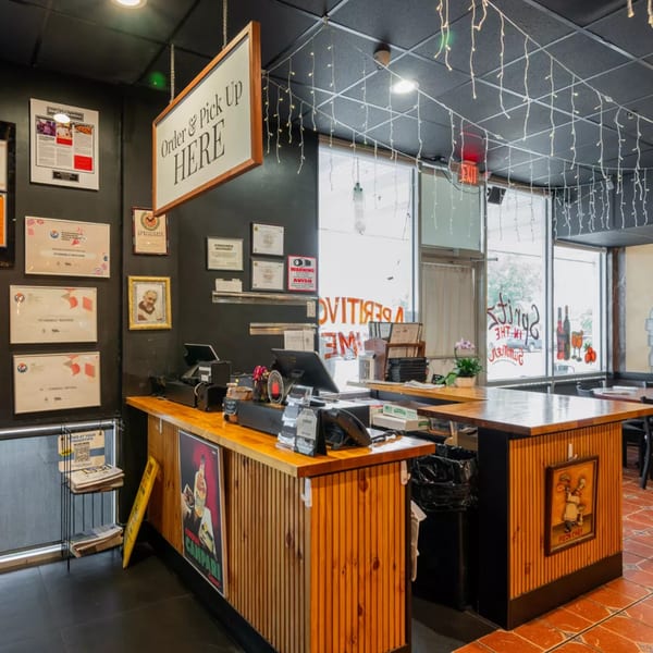 A restaurant's order and pick-up counter with a sign, awards, and string lights.