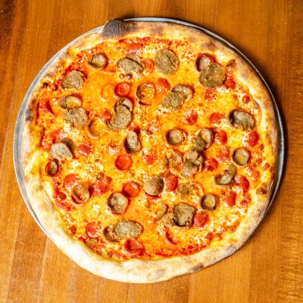 A whole pepperoni and sausage pizza on a metal tray, centered on a wooden table.