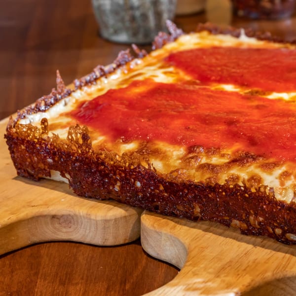 Close-up of a square deep-dish pizza with bright red sauce and crispy cheese crust on a wooden board.