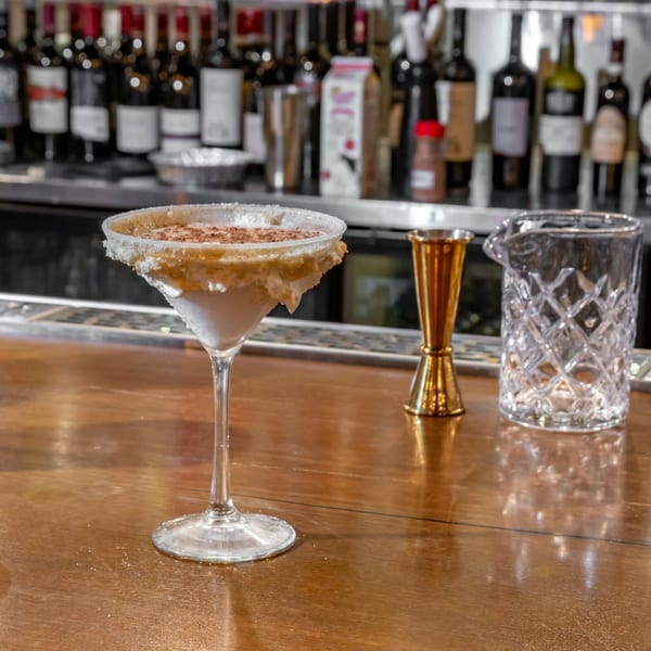 A martini glass with a creamy drink, sugar rim, and cinnamon sits on a bar.