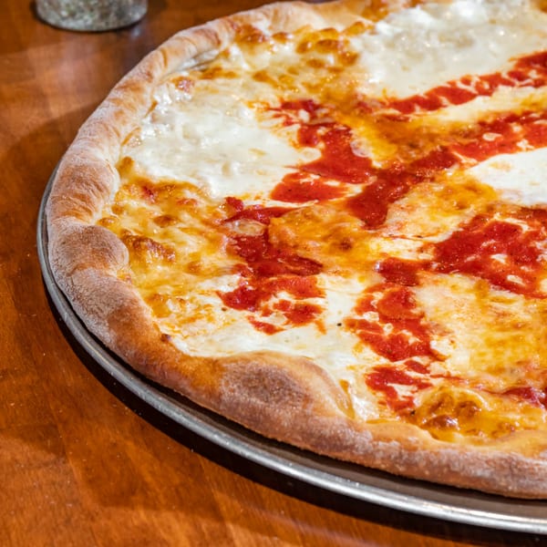 Close-up of a Bella Napoli Pizzeria & Restaurant cheese pizza with red sauce swirls on a metal tray.