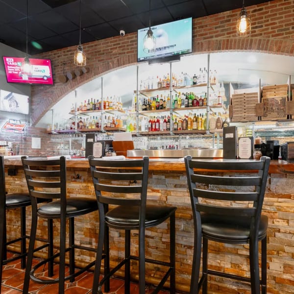 A cozy bar area with brick walls, a fully stocked liquor shelf, and several bar stools.