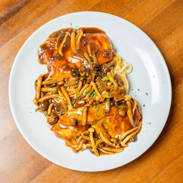 Chicken and pasta covered in a rich mushroom gravy, garnished with parsley on a white plate.
