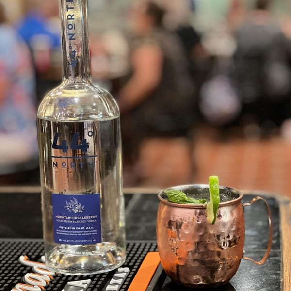 A bottle of 44 North Mountain Huckleberry Vodka next to a copper mug cocktail with lime and mint.