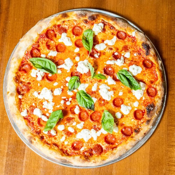 A whole pepperoni pizza with dollops of ricotta cheese and fresh basil leaves on a wooden table.