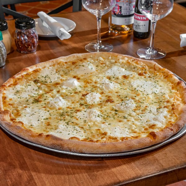 A large white pizza with ricotta cheese and herbs on a wooden table at Bella Napoli Pizzeria.